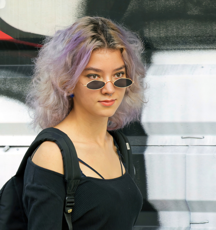 10 - A person wearing small retro oval sunglasses and a black cold-shoulder top paired with a black backpack